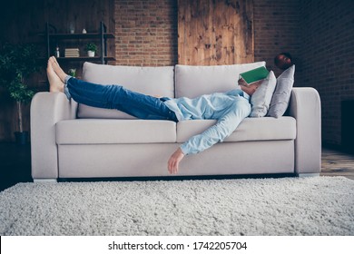 Full size profile photo of domestic handsome guy stay home quarantine time fall asleep reader book cover face lying barefoot cozy sofa daydream modern interior living room indoors - Powered by Shutterstock