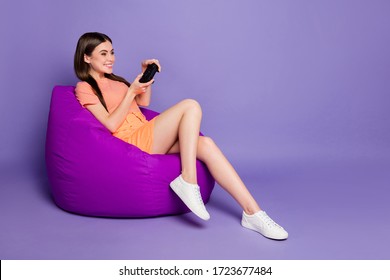 Full size profile photo of funny cheerful lady sitting comfy bean bag playing video games wear casual orange striped t-shirt jeans mini skirt isolated pastel purple color background