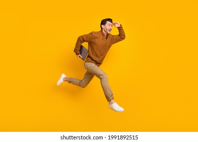 Full size profile photo of impressed nice brunet man hold laptop run wear sweater isolated on yellow background