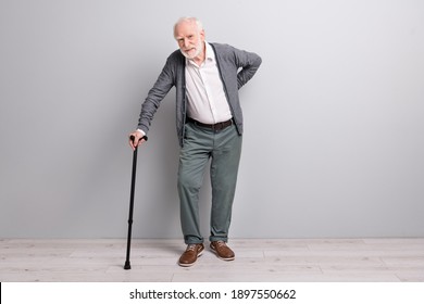 Full Size Profile Photo Of Old Sad Man Touch Back Stand With Wand Wear Dark Sweater Trousers Isolated On Grey Wall