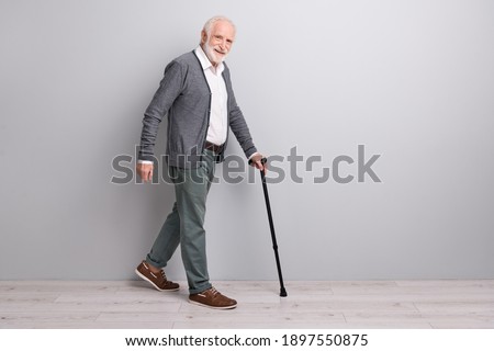 Full size profile photo of optimistic old man go with wand wear dark sweater trousers isolated on grey wall