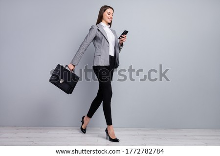 Full size profile photo of slim pretty business lady young chief hold diplomat bag browsing telephone go meeting wear plaid blazer trousers high-heels isolated grey color background