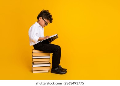 Full size profile photo of small clever schoolchild sit pile stack book read empty space isolated on yellow color background