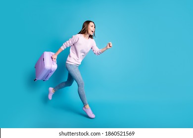 Full size profile side photo cheerful crazy girl enjoy borders open hold suitcase jump run airport check-in travel wear lilac violet sweater denim jeans isolated blue color background