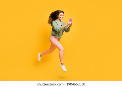 Full size profile side photo of young happy excited crazy girl run in air using smartphone isolated on yellow color background