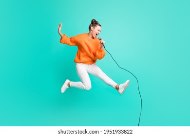 Full size profile side photo of young crazy screaming girl jumping singing in microphone isolated on turquoise color background