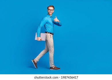 Full Size Profile Side Photo Of Young Man Happy Smile Go Walk Show Thumb-up Advert Advise Laptop Isolated Over Blue Color Background