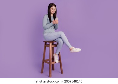Full size profile side photo of young girl look browse cellphone sit stool isolated over purple color background