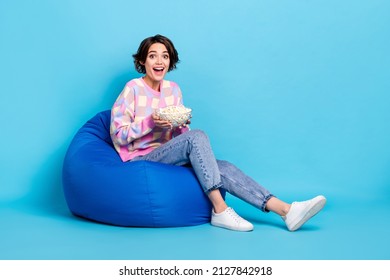 Full size profile side photo of young girl sit beanbag eat pop corn watch film isolated over blue color background