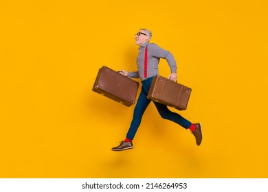 Full size profile side photo of energetic grey haired excited funny pensioner traveling with old valise isolated on yellow color background