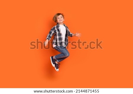 Full size profile side photo of young cheerful boy have fun jump up isolated over orange color background