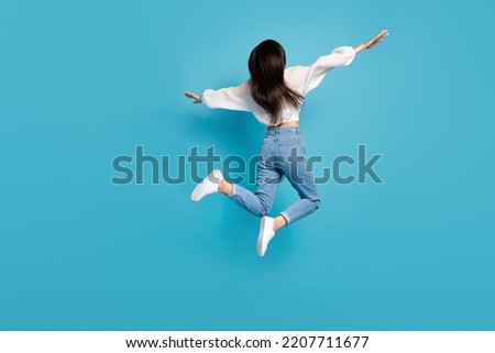 Full size rear behind photo of overjoyed active girl arms wings flying jump isolated on blue color background