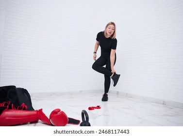 Full size shot of an European young sporty woman 30s, in black sports clothes, standing against white wall background. Sports equipment on the foreground. People, fitness and sport concept - Powered by Shutterstock