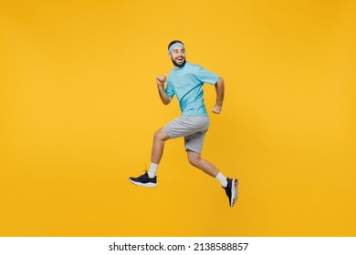 Full Size Side View Strong Young Fitness Trainer Instructor Sporty Man Sportsman Wear Headband Blue T-shirt Jump High Run Fast Look Aside Isolated On Plain Yellow Background. Workout Sport Concept.