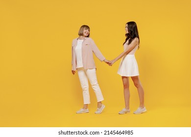 Full Size Side View Two Young Smiling Happy Daughter Mother Together Couple Women Wear Casual Beige Clothes Hold Hands Walk Like Follow Me Isolated On Plain Yellow Color Background Studio Portrait.