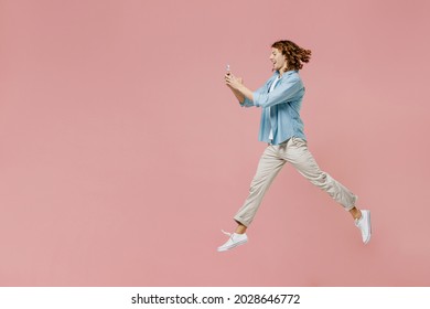 Full size side view young excited happy man 20s with long curly hair wear blue shirt white t-shirt using hold in hand mobile cell phone jump high isolated on pastel plain pink color background studio. - Powered by Shutterstock