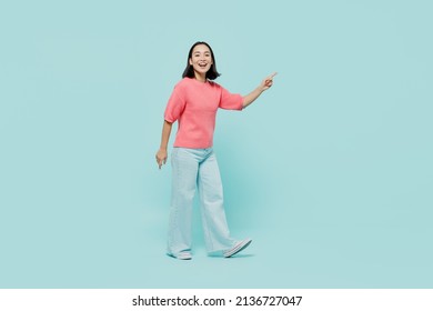 Full Size Side View Young Smiling Happy Woman Of Asian Ethnicity 20s Wearing Pink Sweater Walk Going Point Index Finger Aside On Workspace Area Isolated On Pastel Plain Light Blue Background Studio.