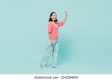 Full Size Side View Young Smiling Happy Woman Of Asian Ethnicity 20s Wearing Pink Sweater Walk Going Waving Hand Isolated On Pastel Plain Light Blue Color Background Studio. People Lifestyle Concept