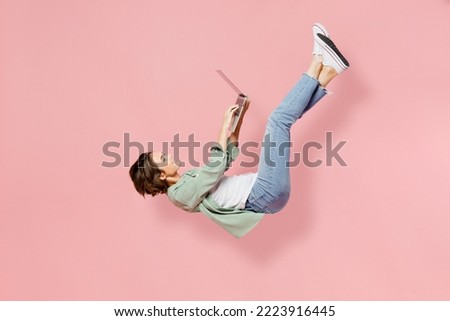 Full size side view young happy IT woman she wear green shirt white t-shirt fly up hover over air fall down hold use work on laptop pc computer isolated over plain pastel light pink background studio