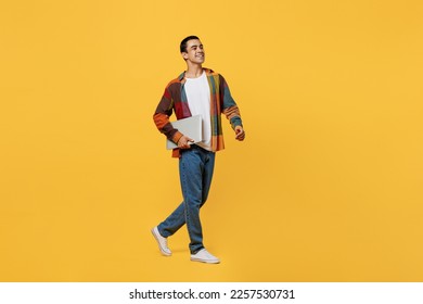 Full size smiling happy young middle eastern IT 20s wear casual shirt white t-shirt hold closed laptop pc computer walk go isolated on plain yellow background studio portrait People lifestyle concept - Shutterstock ID 2257530731