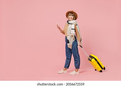 Full Size Traveler Tourist Fun Mature Elderly Woman 55 Years Old Wear Casual Clothes Hat Scarf Hold Suitcase Bag Use Mobile Cell Phone Go Isolated On Plain Pastel Light Pink Background Studio Portrait