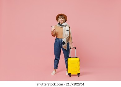 Full Size Traveler Tourist Mature Elderly Lady Woman 55 Years Old Wears Casual Clothes Hat Scarf Hold Suitcase Bag Use Mobile Cell Phone Isolated On Plain Pastel Light Pink Background Studio Portrait