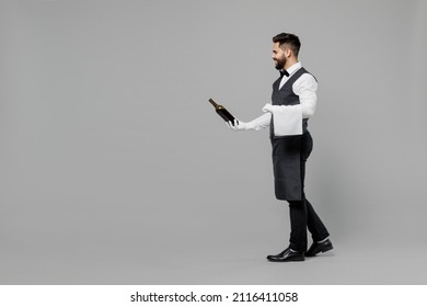 Full Size Young Barista Male Waiter Butler Man 20s Wear White Shirt Vest Elegant Uniform Work At Cafe Give Bottle Of Wine Isolated On Plain Grey Background Studio Portrait. Restaurant Employee Concept