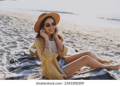 Full size young happy traveler tourist woman in straw hat glasses shirt summer clothes wireless earphones listen to music outdoors on sea beach background People vacation lifestyle journey concept. - Powered by Shutterstock