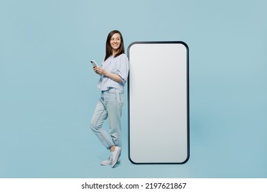Full size young happy woman she 20s in casual blouse big huge blank screen mobile cell phone with workspace copy space mockup area hold smartphone isolated on pastel plain light blue background studio - Shutterstock ID 2197621867