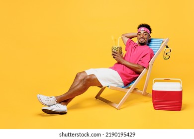 Full Size Young Man He Wear Pink T-shirt Bandana Lying On Deckchair Near Hotel Pool Drink Pineapple Juice Hold Hand Behind Neck Isolated On Plain Yellow Background. Summer Vacation Sea Rest Concept