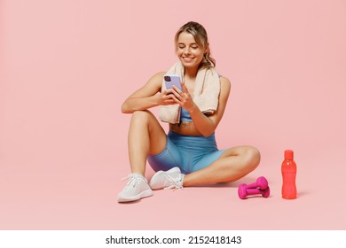 Full size young sporty fitness trainer instructor woman wear blue tracksuit spend time in home gym sit on floor use mobile cell phone isolated on plain light pink background. Workout sport concept. - Powered by Shutterstock