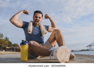 Full size young sporty strong toned fit sportsman man in sports clothes towel training near water bottle show biceps muscles at sunrise sun over sea beach outdoor on pier seaside in summer day morning - Powered by Shutterstock