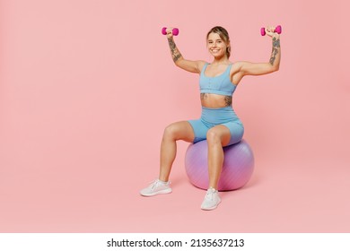 Full size young strong sporty athletic fitness trainer instructor woman wear blue tracksuit spend time in home gym sit on fitball isolated on pastel plain light pink background. Workout sport concept