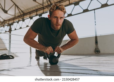 Full size young strong sporty athletic toned fit sportsman man 20s in sports clothes warm up training work out engaged with kettlebell at outdoor gym sea beach outdoor seaside in summer day morning. - Powered by Shutterstock