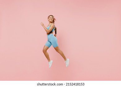 Full size young strong sporty athletic fitness trainer instructor woman wear blue tracksuit spend time in home gym jump high run isolated on pastel plain light pink background. Workout sport concept