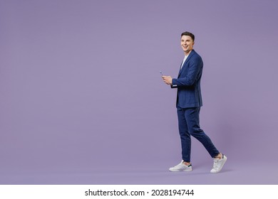 Full size young successful employee business man lawyer 20s wear formal blue suit white t-shirt work in office move stroll hold use mobile cell phone isolated pastel purple background studio portrait
