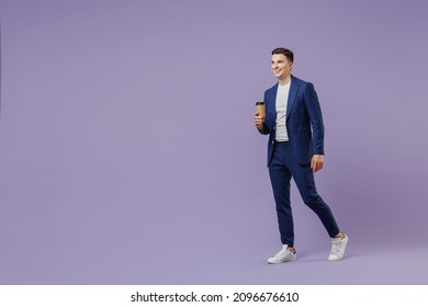 Full size young successful employee business man lawyer 20s wear formal blue suit white t-shirt hold takeaway paper brown cup coffee go look aside isolated on pastel purple background studio portrait