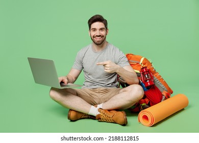 Full Size Young Traveler White Man Near Backpack Mat Sit Use Work Point On Laptop Pc Computer Isolated On Plain Green Background. Tourist Leads Active Lifestyle. Hiking Trek Rest Travel Trip Concept