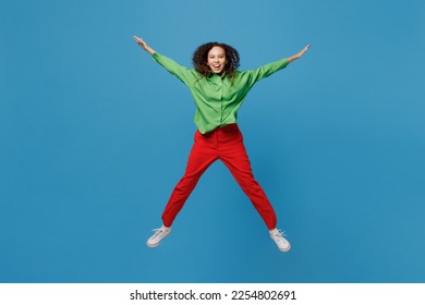 Full size young woman of African American ethnicity 20s wear green shirt jump high with outsretched hands legs like flying isolated on plain blue background studio portrait. People lifestyle concept - Shutterstock ID 2254802691