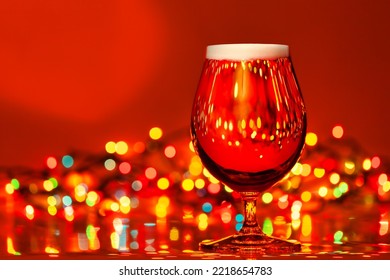 Full Snifter Glass Of Lager Beer With Blurred Christmas Lights On Red Background