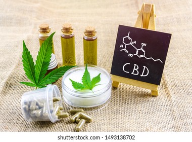 Full spectrum CBD and THC cannabis oils, pills and cbd lotion on hemp cloth with chemical structure on blackboard
