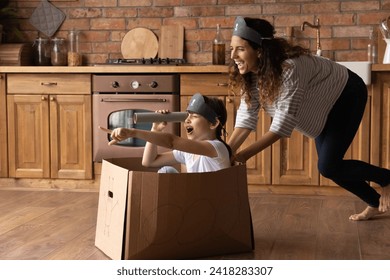 Full speed ahead. Laughing young latina mother enjoy pretending pirate with little daughter push girl around kitchen in ship made of box. Joyful adult elder and younger sisters play funny game at home - Powered by Shutterstock