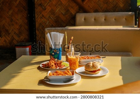 Full table setup of fast food assortment including pasta, chicken fry, burger, and milkshakes in a cozy restaurant booth