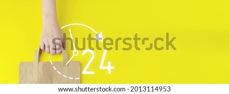 Full time service concept. Recycled brown paper shopping bag in hand with hologram 24 7 all day all night icon on yellow background, flat lay. Summer sale concept. Delivery service concept.