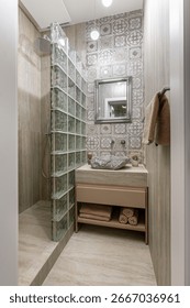 A full view of a compact rustic bathroom with a stone sink, vintage patterned tiles, a framed mirror, and a walk-in shower enclosed by green glass blocks.