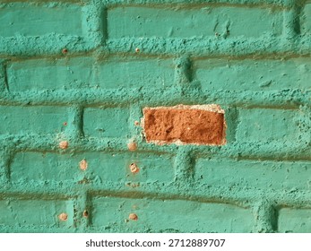 A full view of a wall featuring a pattern of heavily painted turquoise teal bricks, with one central, exposed red brick creating a focal point of high color and texture contrast