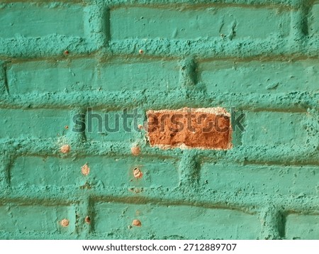 A full view of a wall featuring a pattern of heavily painted turquoise teal bricks, with one central, exposed red brick creating a focal point of high color and texture contrast