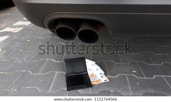 A full wallet\
under an exhaust from a car.