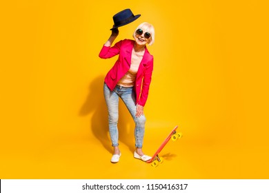 Full-body full-legh portrait of happy granny with a board for skating isolated on vivid yellow background