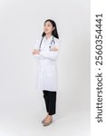 A full-body portrait of a beautiful Asian female doctor in a white gown uniform standing with her arms crossed against a white studio background. people and medical concepts